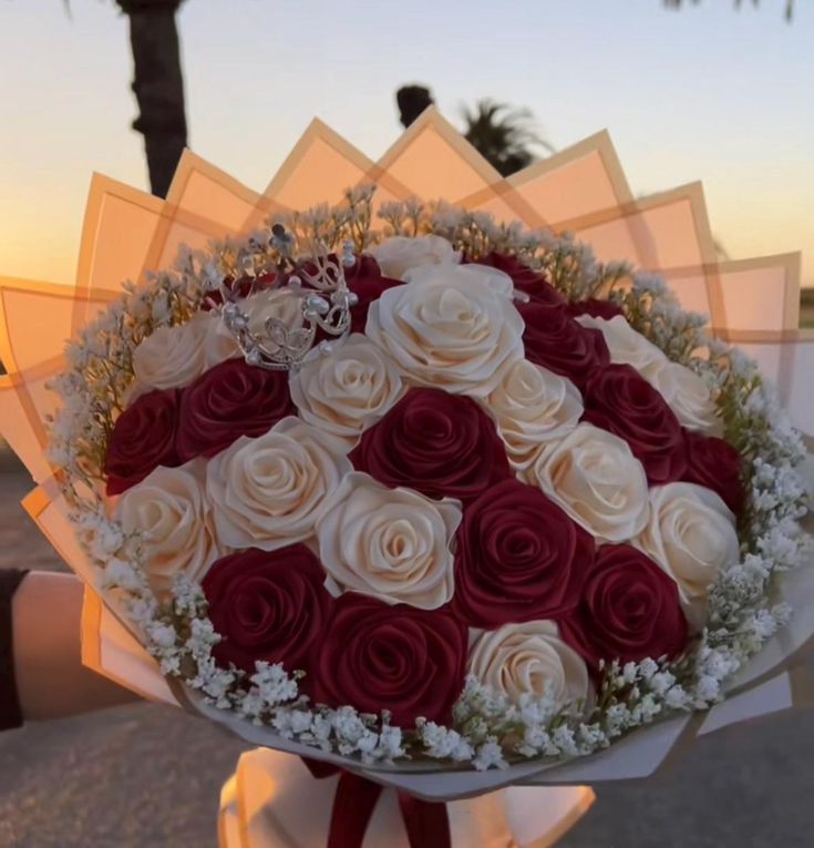 a bouquet of red and white roses in someone's hand with the sun setting behind them