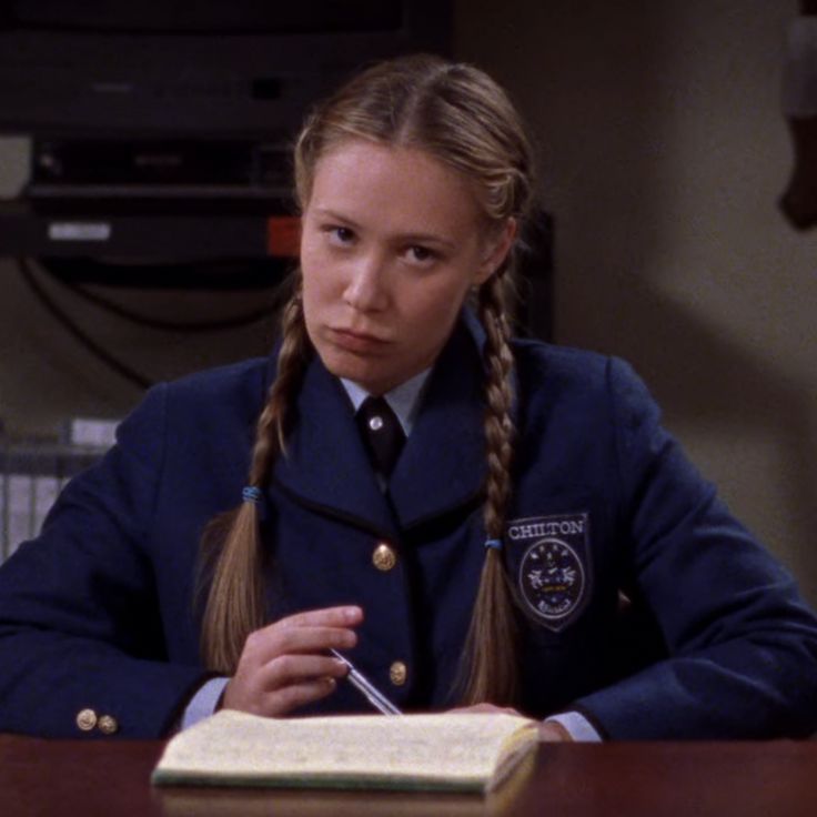 a woman in uniform sitting at a desk with an open book and pen on her lap