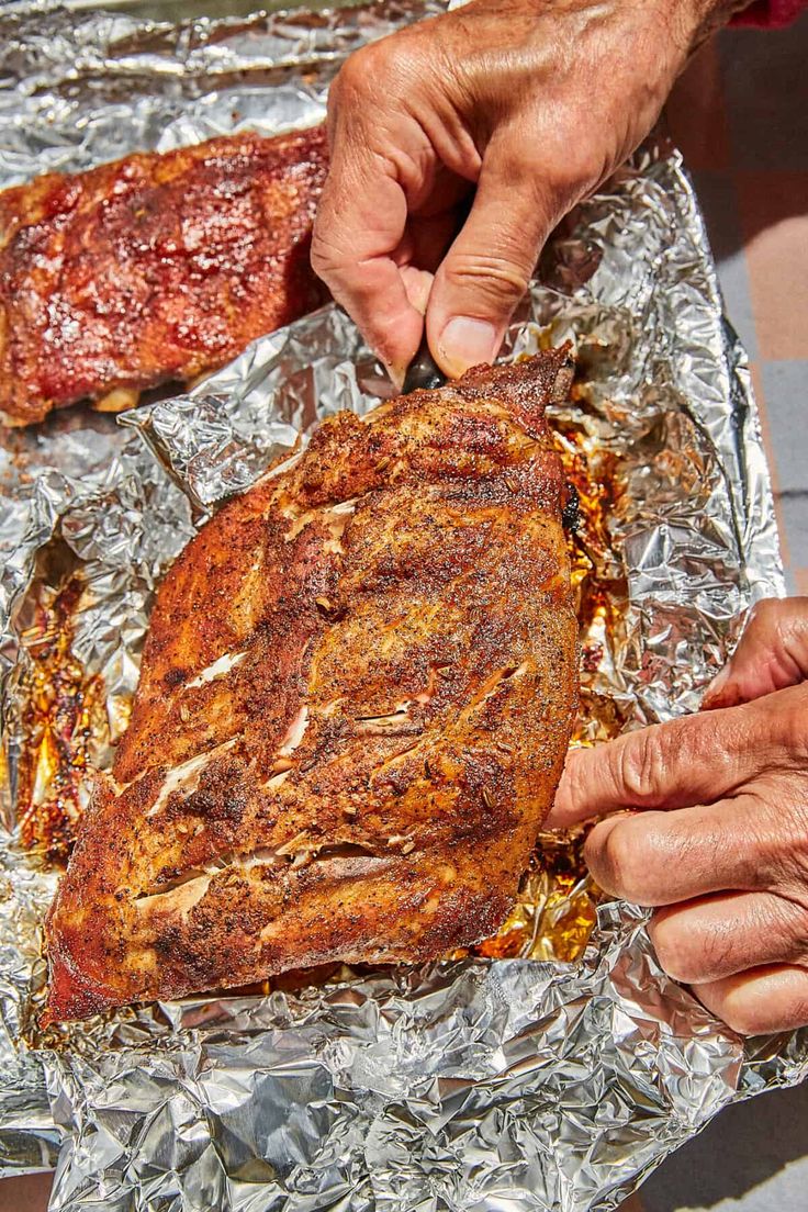 two hands are touching the ribs on tin foil