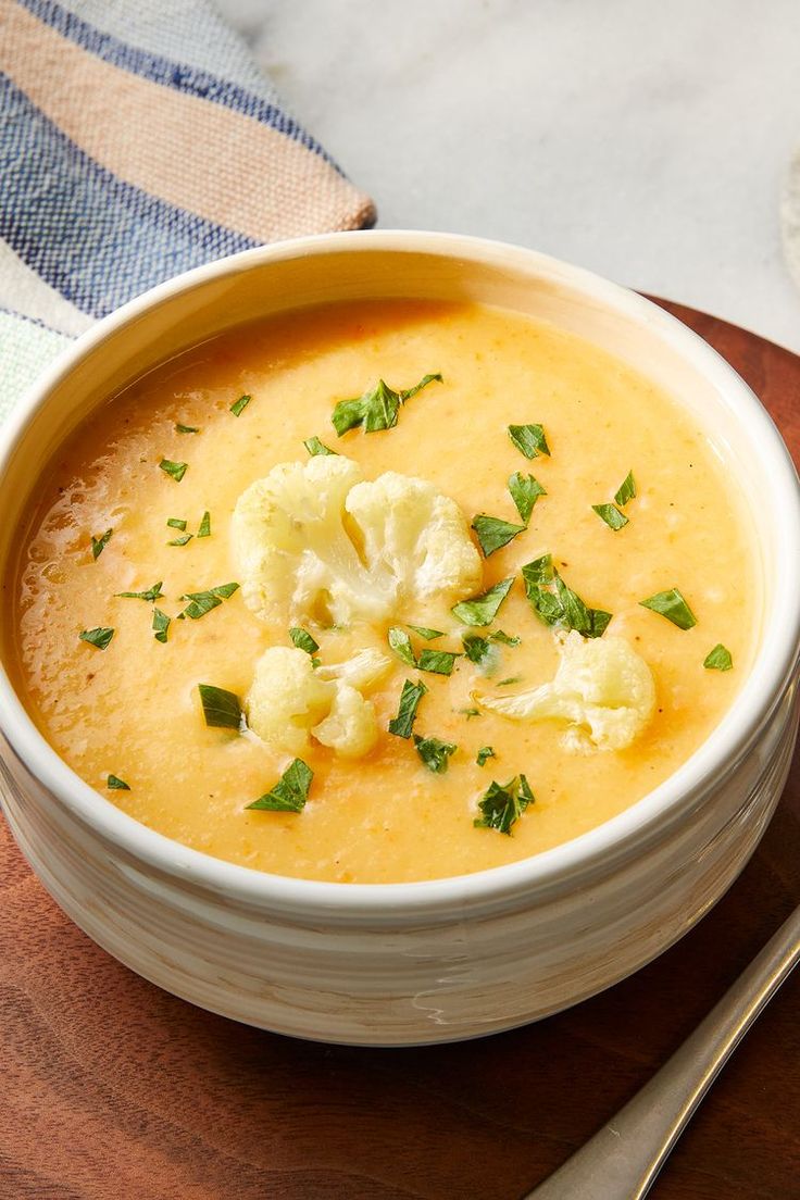 a bowl of soup with cauliflower and parsley on the side next to a spoon