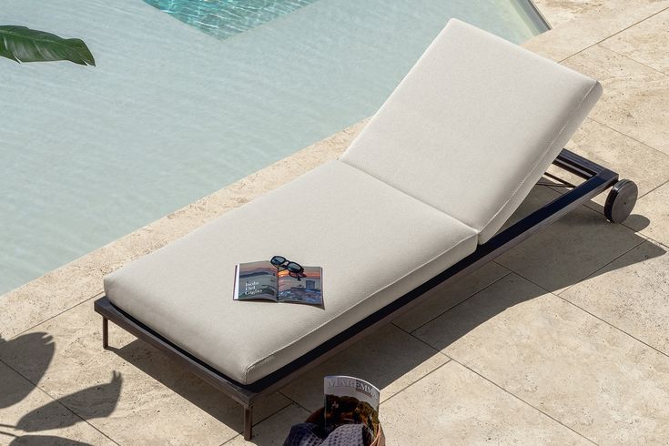 a person laying on a chaise lounge next to a swimming pool with a magazine