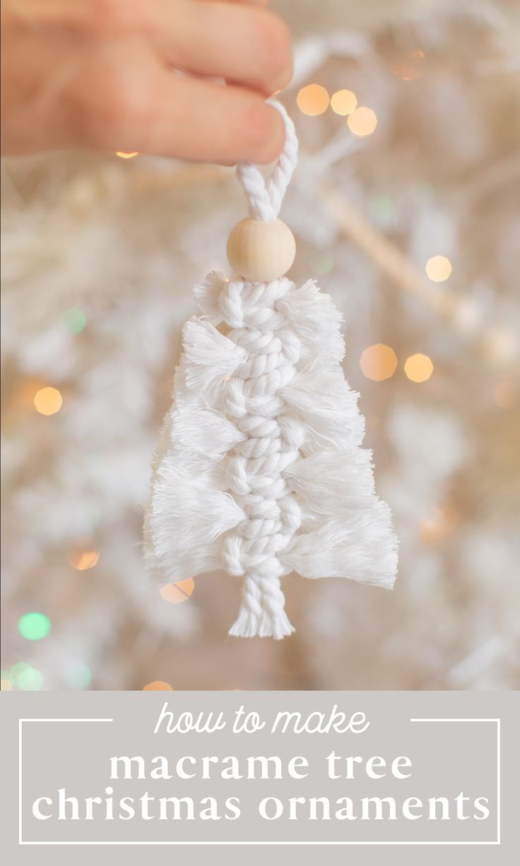 a hand holding a white christmas ornament in front of a tree