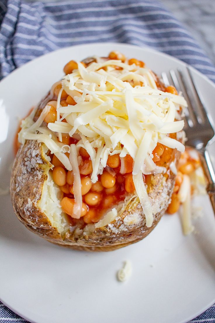 a baked potato covered in cheese and beans on a plate with a fork next to it