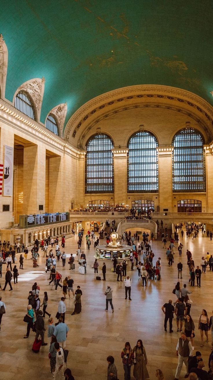 many people are walking around in an indoor area with large windows and green ceilinging