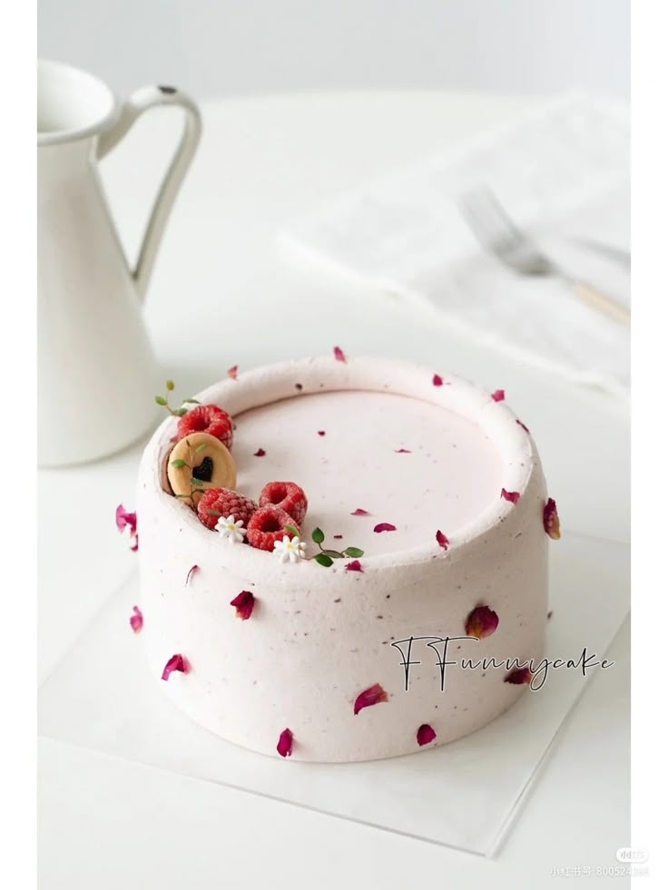 a white cake with raspberries and flowers on it sitting next to a coffee mug