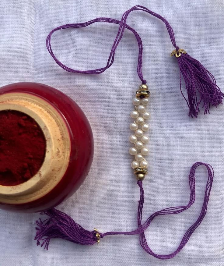 a red vase sitting on top of a table next to a purple tassell