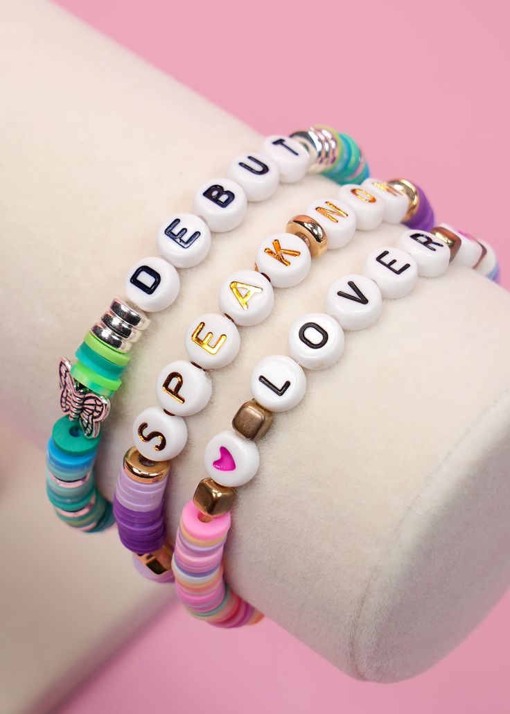 three bracelets with words on them sitting on top of a white display stand in front of a pink background