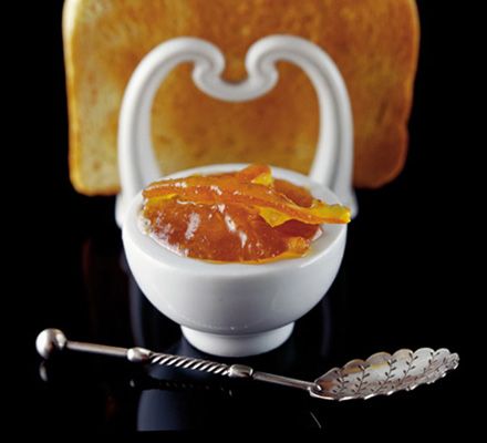 a white bowl filled with orange jelly next to a piece of bread