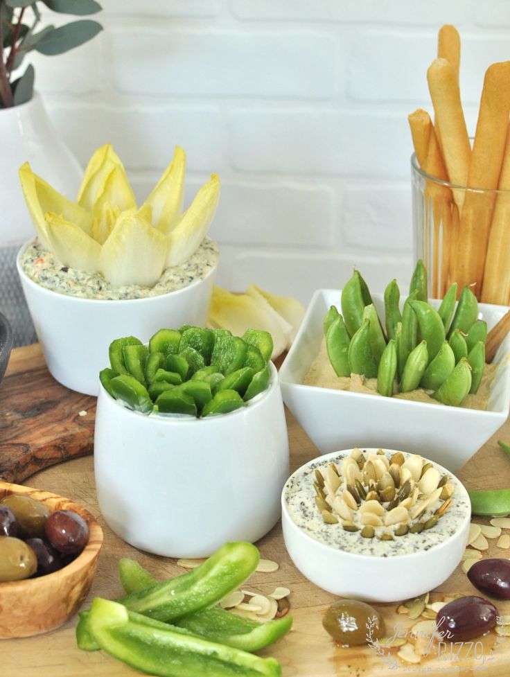 several bowls filled with different types of vegetables on a table next to breadsticks