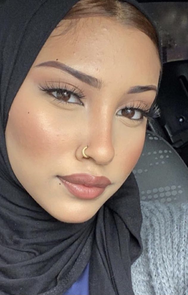 a woman wearing a black hijab and gold nose ring is looking at the camera