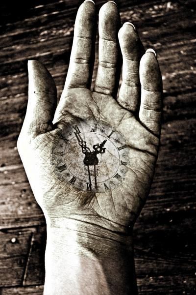 a person's hand with a clock tattoo on the middle of their palm, in front of a wooden wall