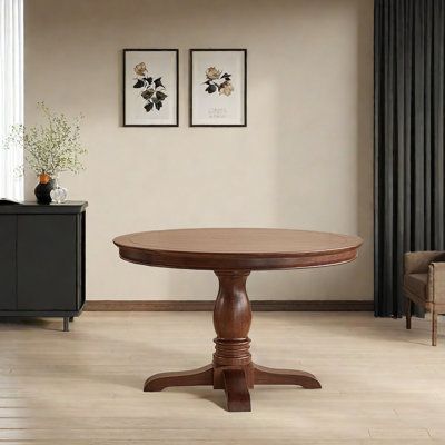 a round wooden table sitting on top of a hard wood floor next to a window