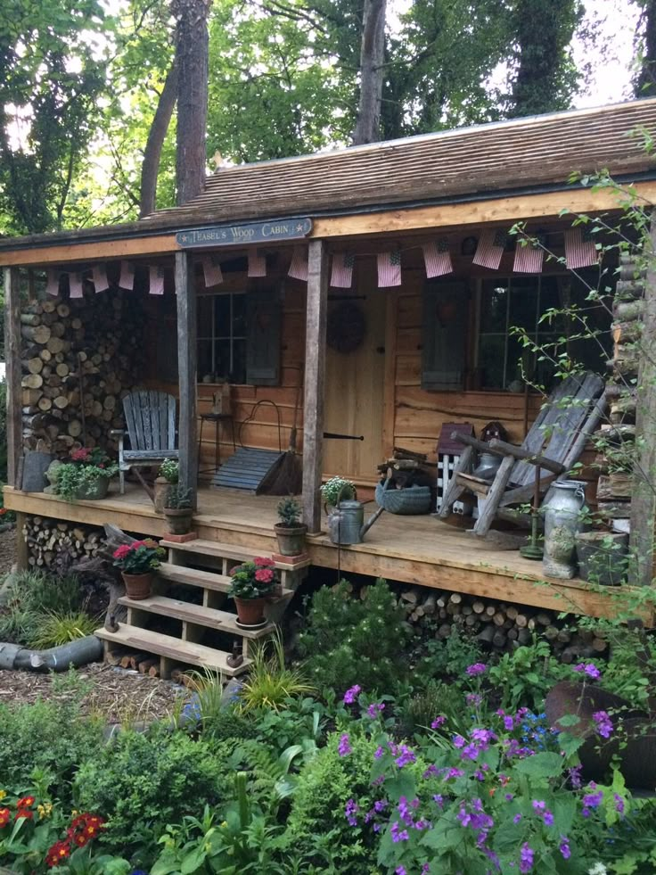 a small wooden cabin sitting in the middle of a lush green forest filled with flowers