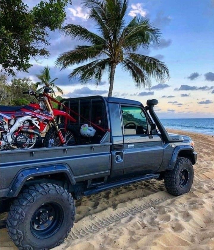 a truck parked on top of a sandy beach next to the ocean and palm trees