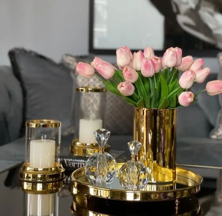 pink tulips are in a gold vase on a mirrored coffee table with candles