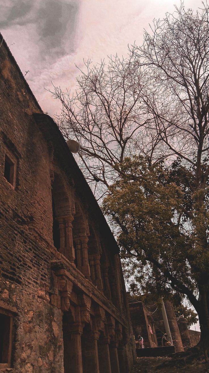 an old stone building with trees in the foreground and cloudy sky above, on a sunny day