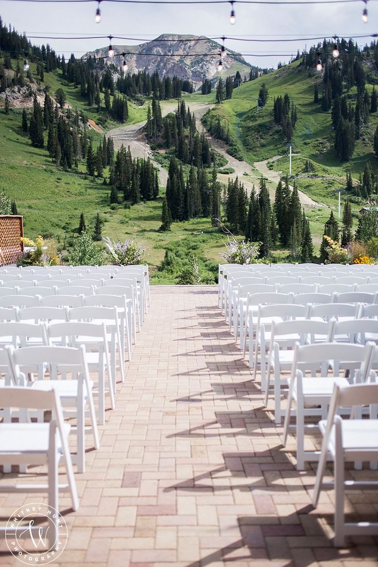 rows of white folding chairs set up for an outdoor wedding ceremony in the mountainside