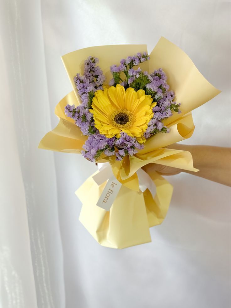 a person holding a bouquet of flowers in their left hand and wearing a yellow ribbon around it