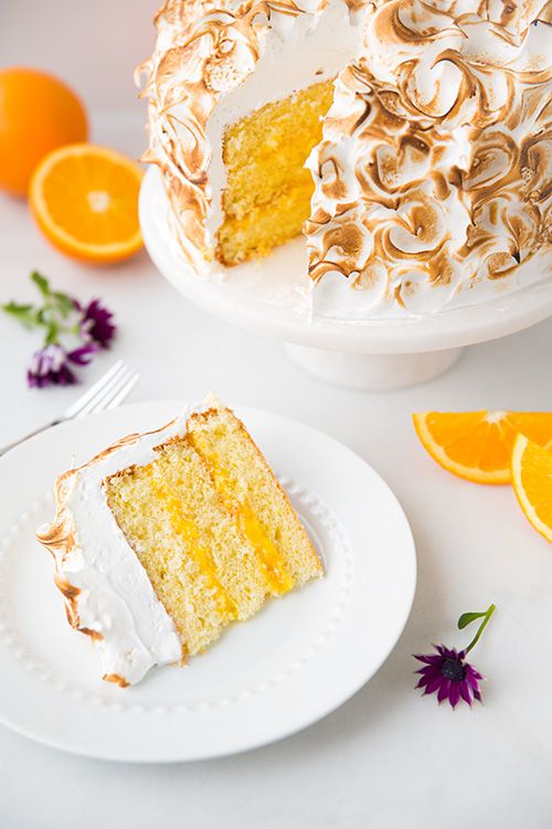 a slice of cake on a plate next to an orange and white cake with icing