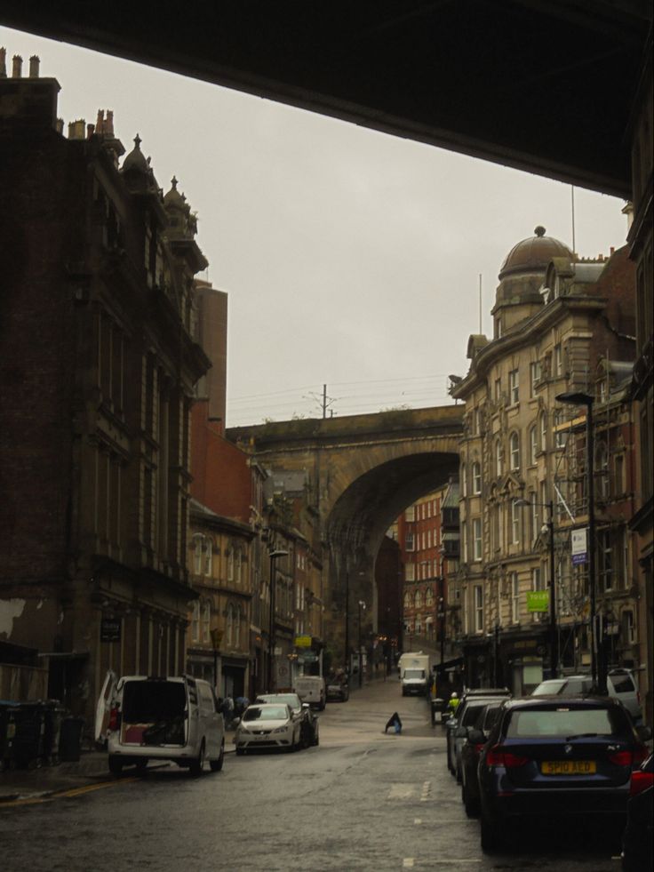 cars are parked on the street in front of buildings and an arched bridge over it