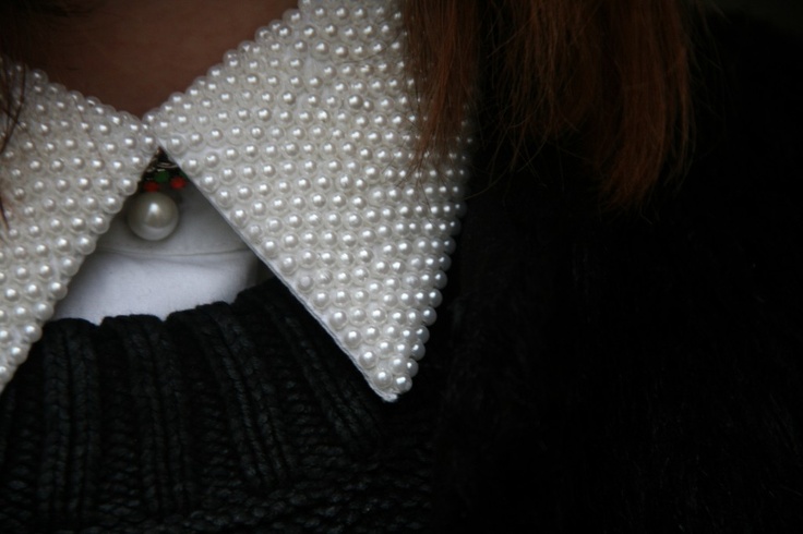 a close up of a person wearing a sweater and tie with pearls on the collar