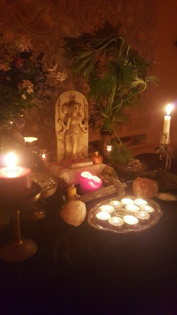 candles are lit in front of a statue and other items on a table with flowers