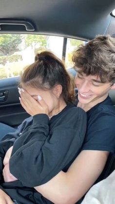 two people sitting in the back seat of a car, one holding his head and smiling