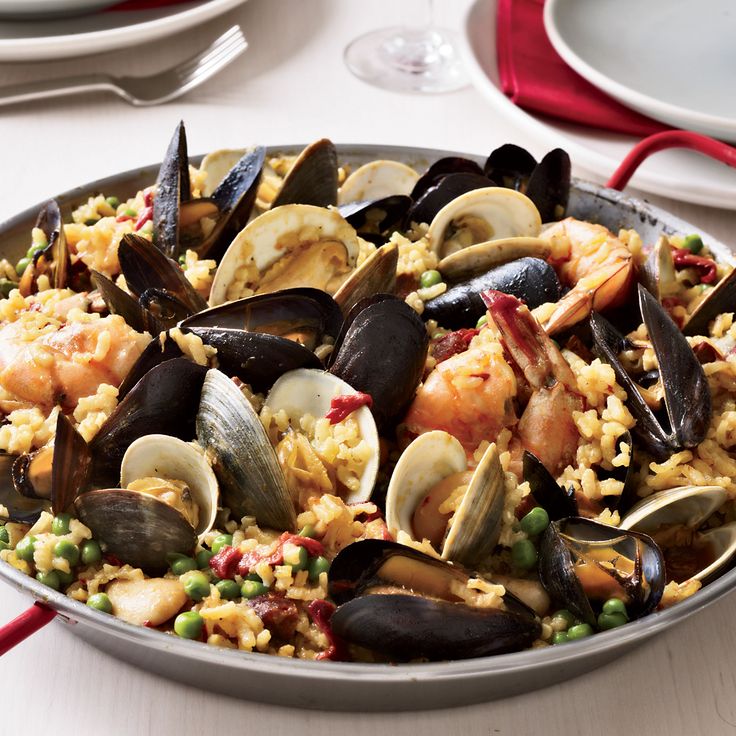 a pan filled with seafood and rice on top of a table next to silverware