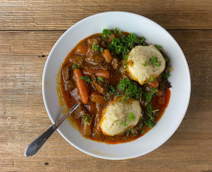 a bowl filled with stew and dumplings on top of a wooden table