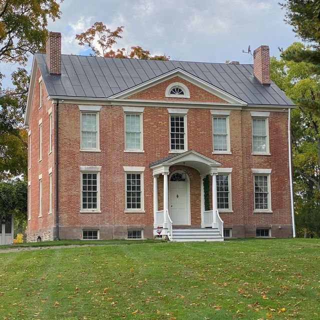 an old red brick house sitting on top of a lush green field