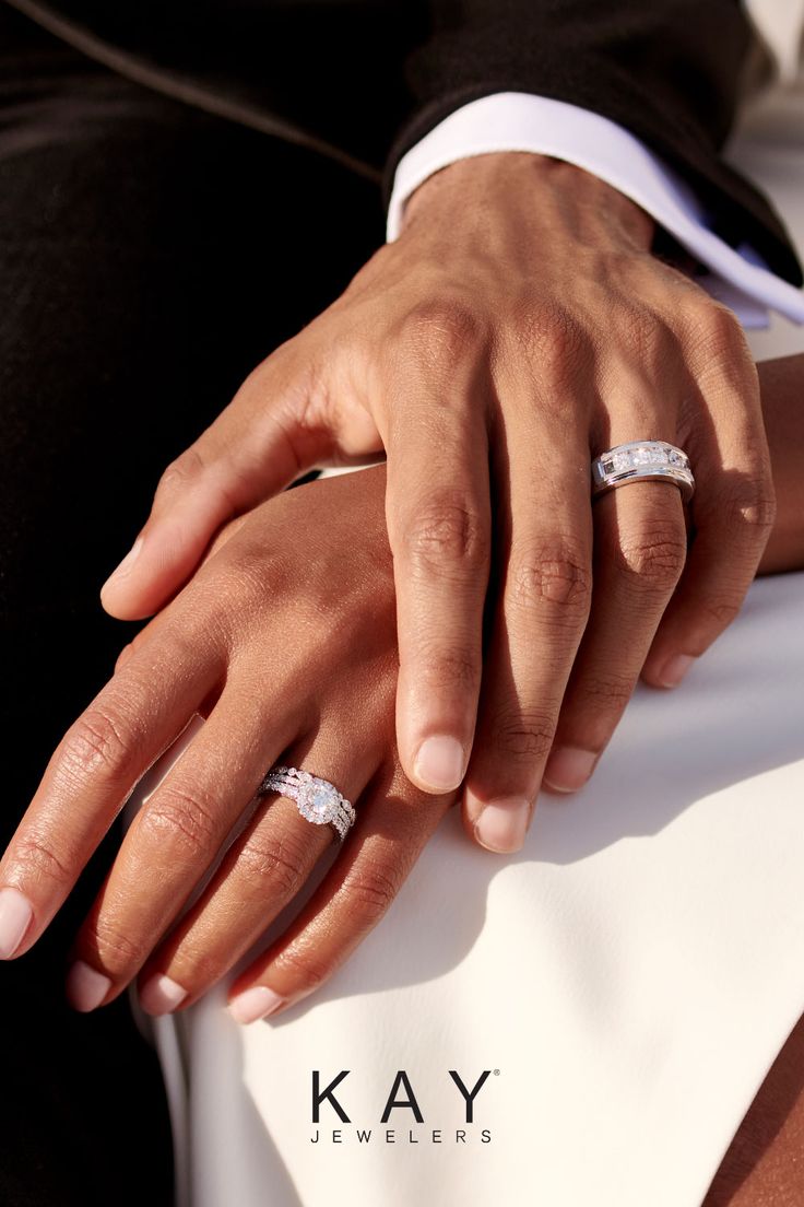 two people wearing wedding rings sitting next to each other with their hands on top of one another