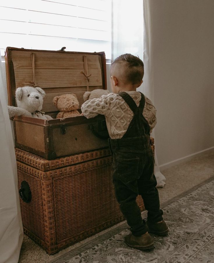 a little boy standing in front of an old trunk with stuffed animals on top of it