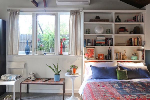 a bed room with a neatly made bed next to a window and bookshelves