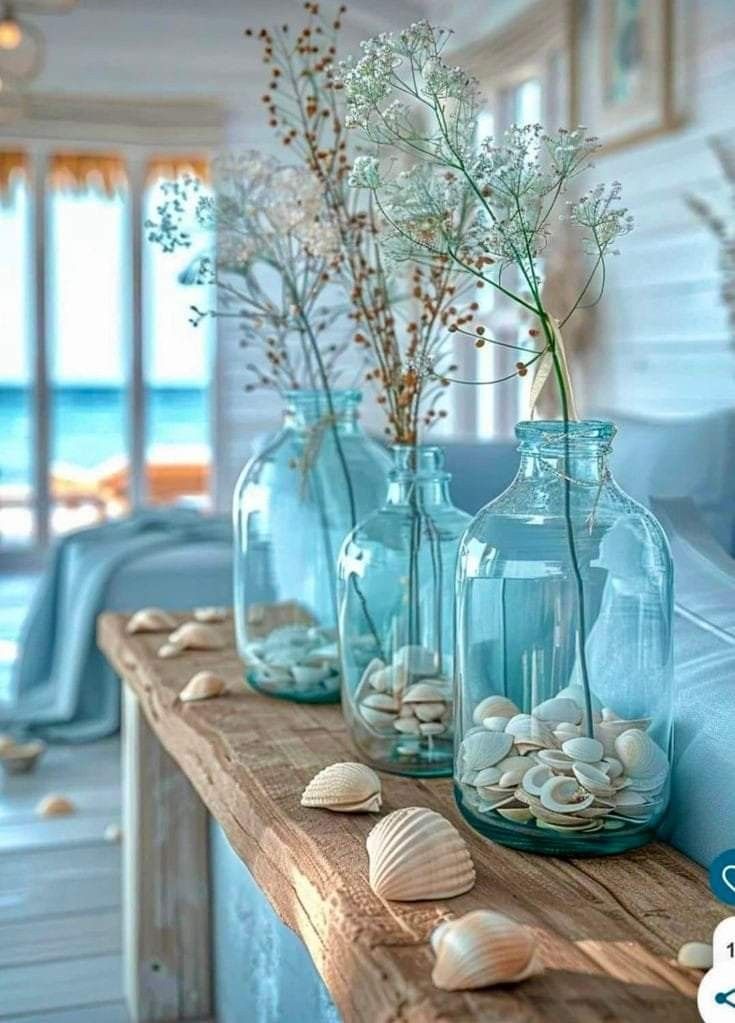 three blue vases filled with sea shells and flowers on a table next to a couch