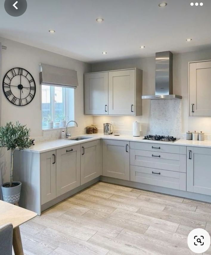 a large kitchen with white cabinets and grey counter tops is shown in this image, the clock on the wall above the stove