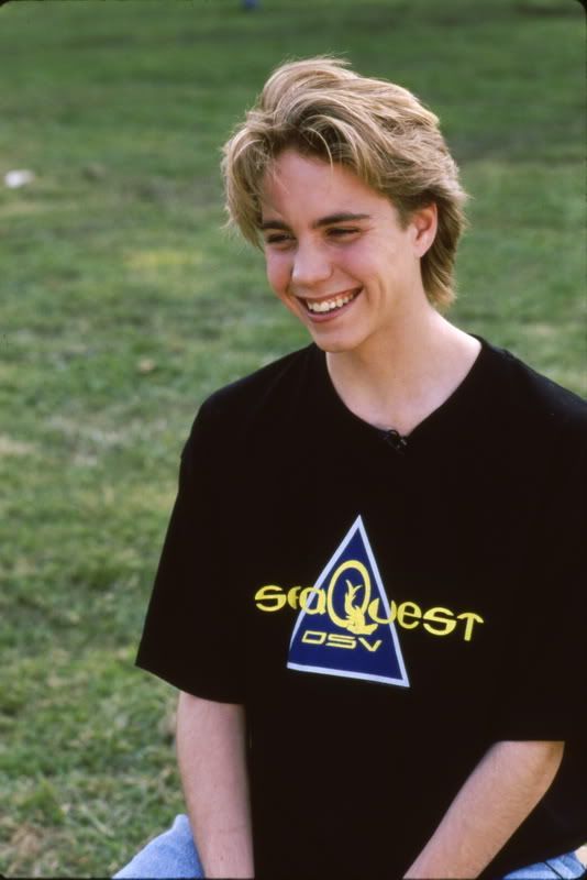 a young man sitting on top of a lush green field