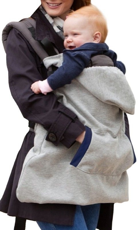 a woman carrying a baby in a grey and black carrier on her back while walking down the street