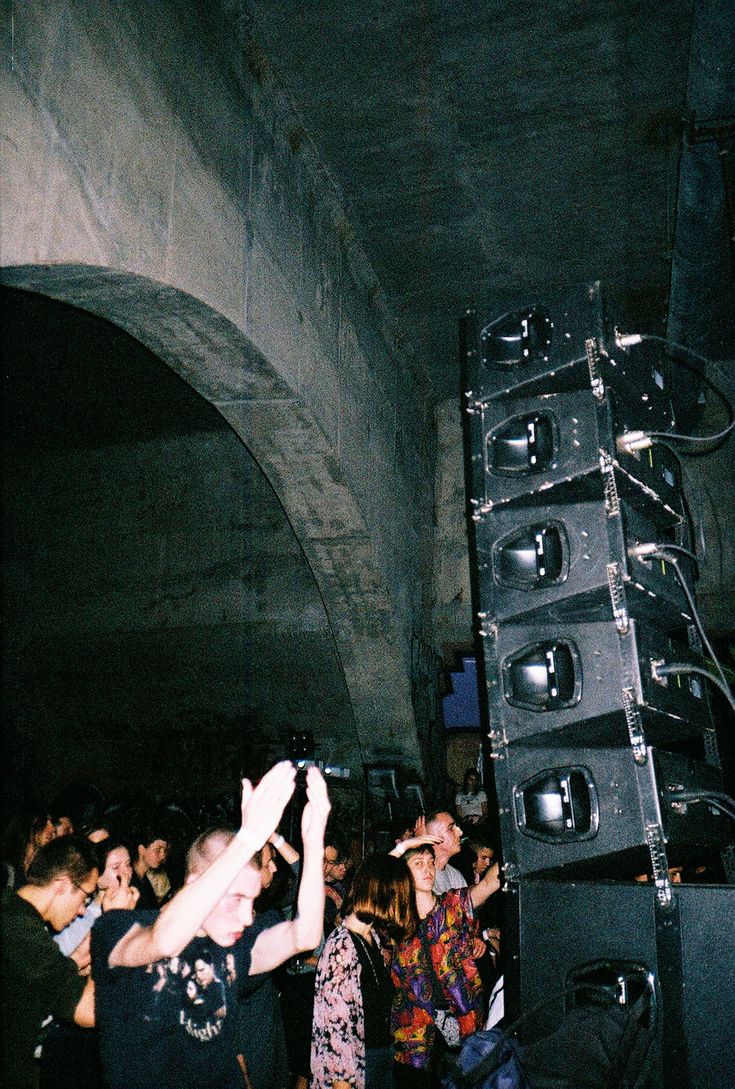 a group of people standing in front of a speaker system on a stage with their hands up