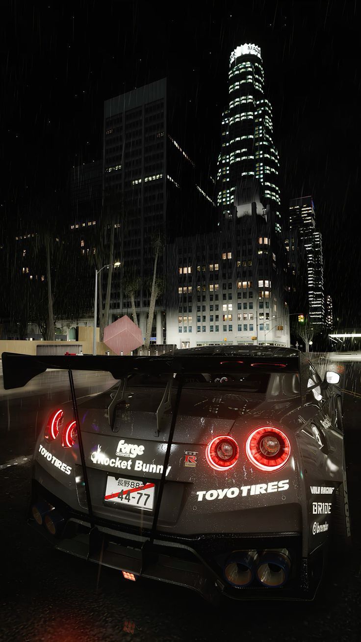 a car parked in front of a tall building with lights on it's windows