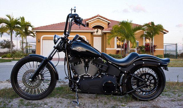 a black motorcycle parked in front of a house with palm trees and bushes behind it