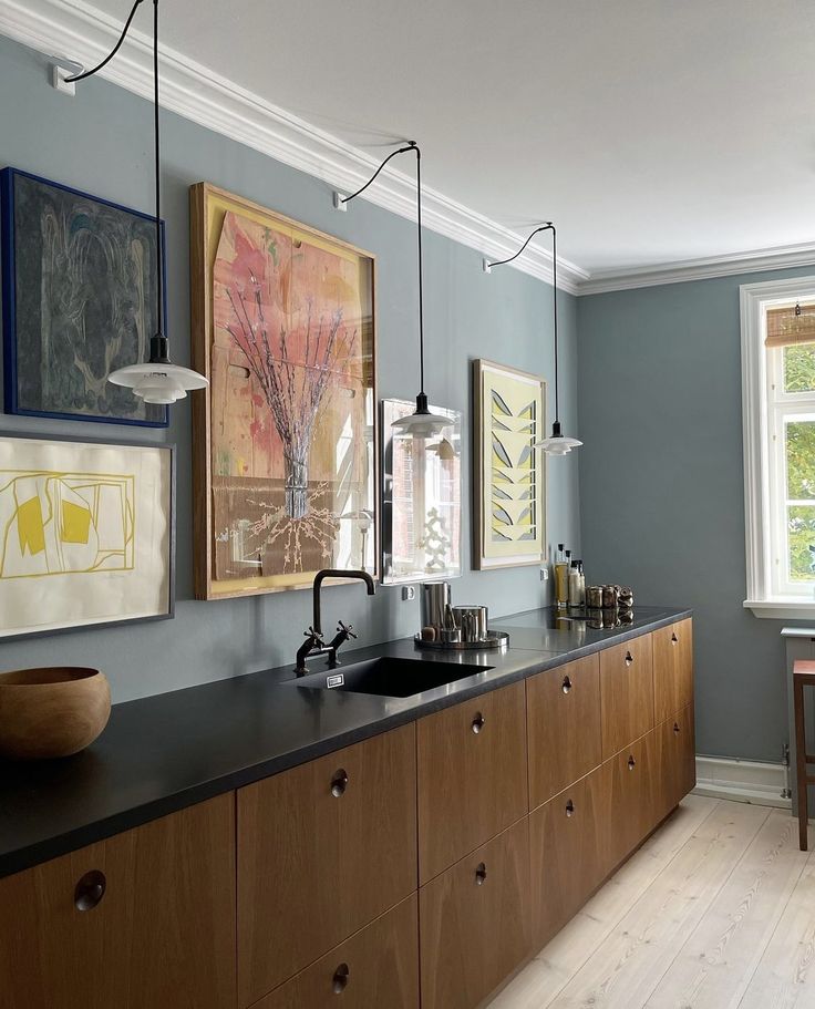 a kitchen with wooden cabinets and black counter tops, artwork on the wall above the sink