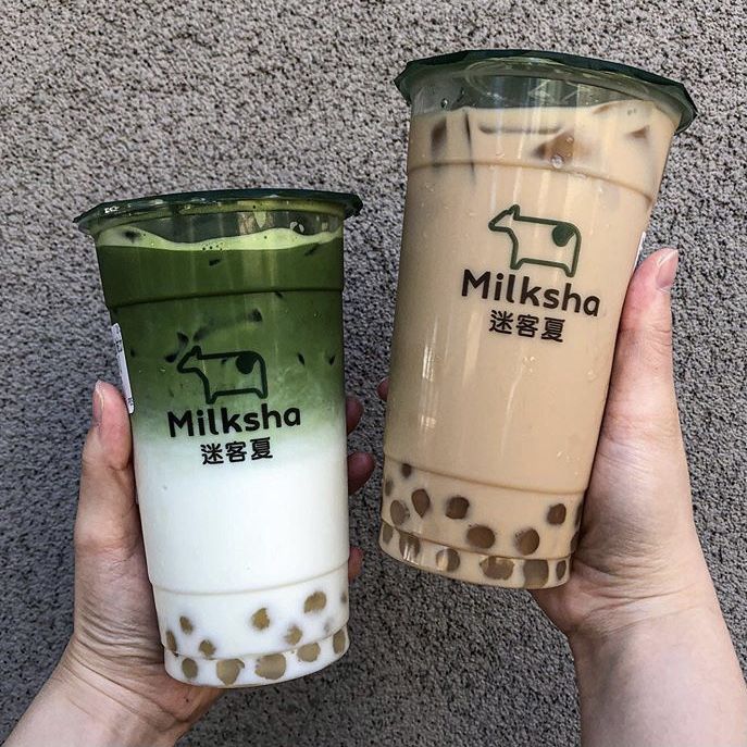 two people holding up cups with milkshakes in them on the floor next to each other