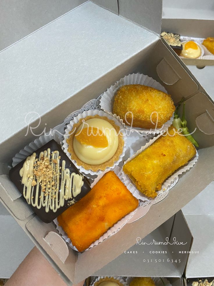 an open box filled with assorted pastries and desserts next to each other