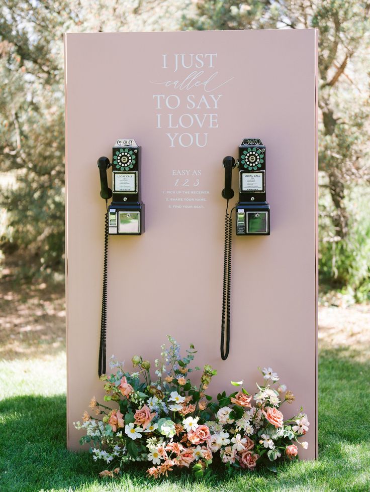 two old fashioned telephones sitting on top of a pink sign with flowers in front of it