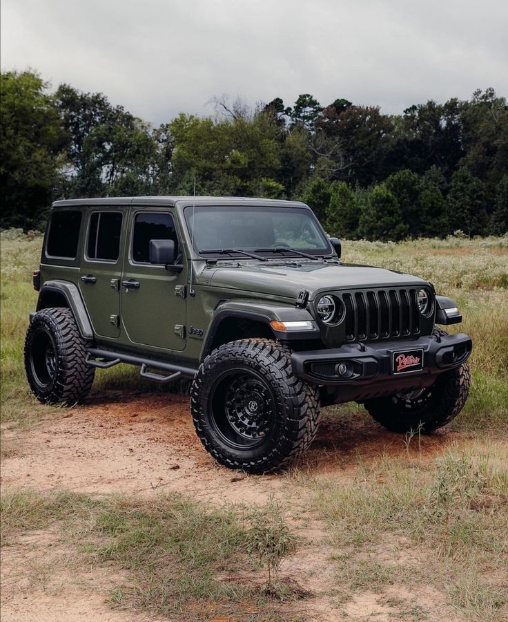 a green jeep parked on top of a dirt road in the middle of a field