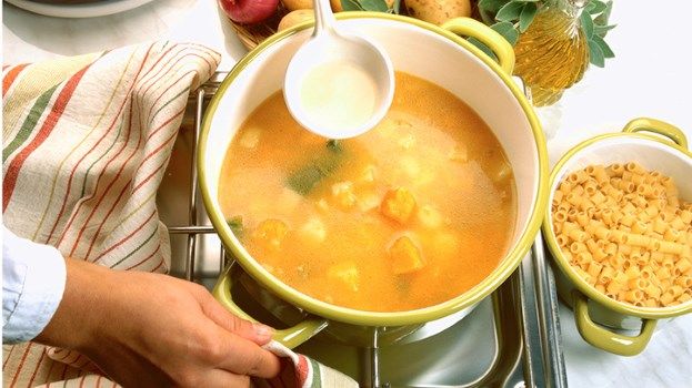 a person pouring soup into a pot on top of a stove next to other dishes