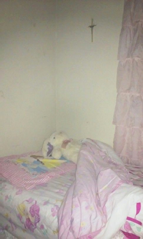 a small bed with pink sheets and a cross on the wall