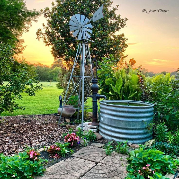 a windmill in the middle of a garden with flowers and plants around it at sunset