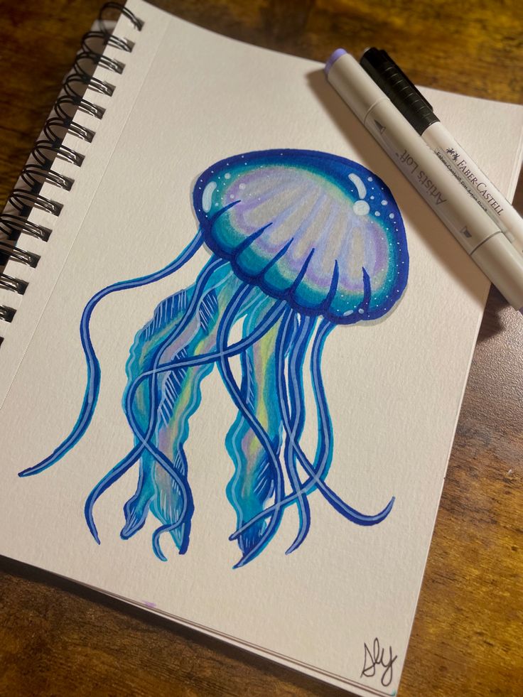 a drawing of a jellyfish with blue watercolors on paper next to a marker