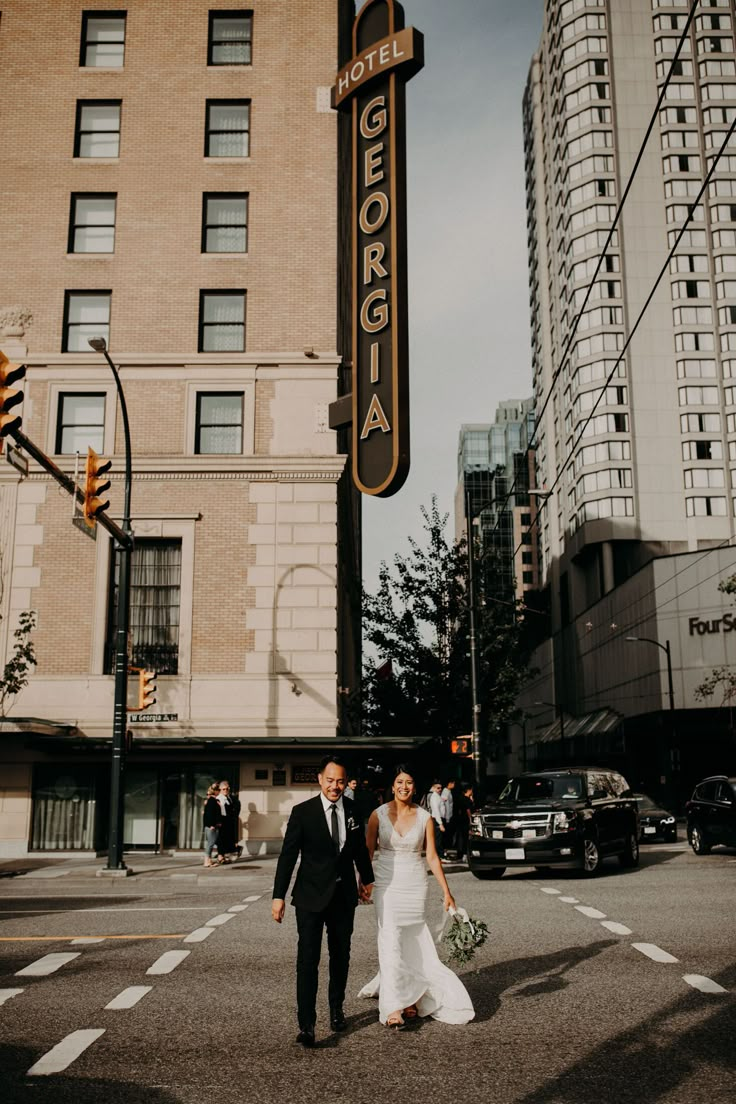 a bride and groom walk across the street in front of an old hotel sign that reads george